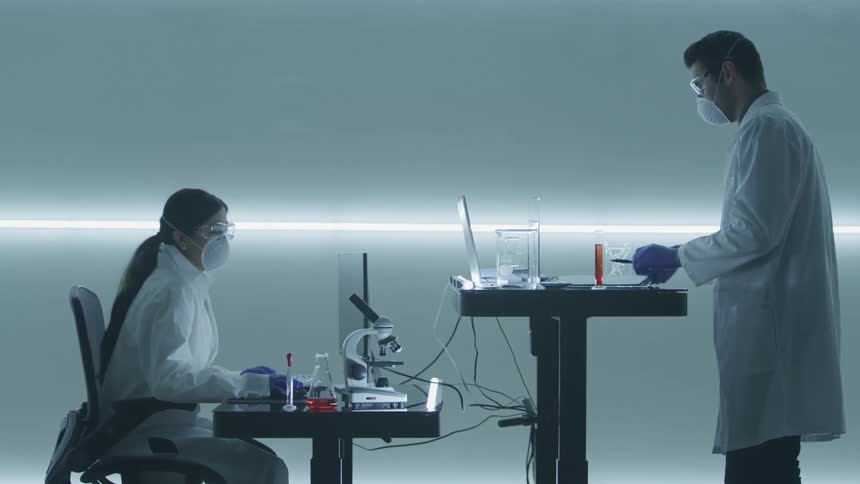 A man and woman medical scientist look at different objects and record findings