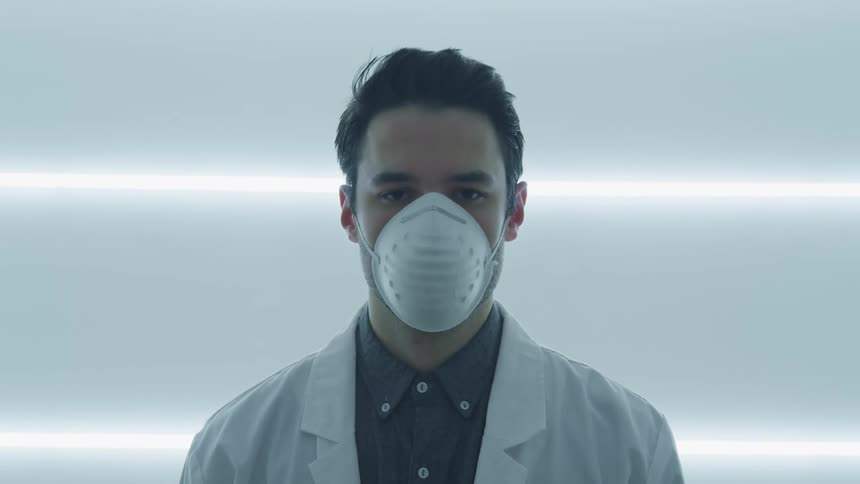 A doctor with a mask on stands in a brightly lit room