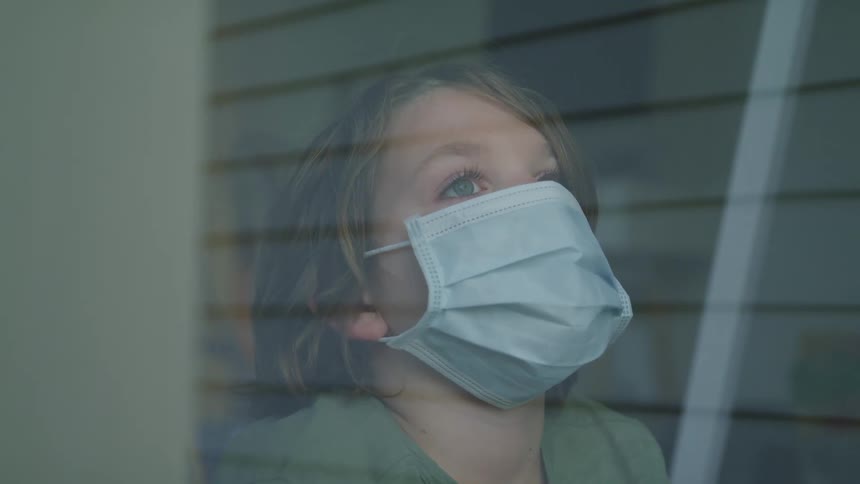 Small blonde boy with blue eyes wearing a blue face mask behind a glass