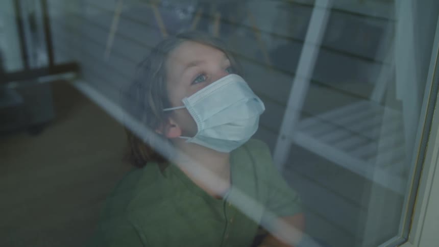Blonde boy with a green t shirt and a blue mask looks up out the window