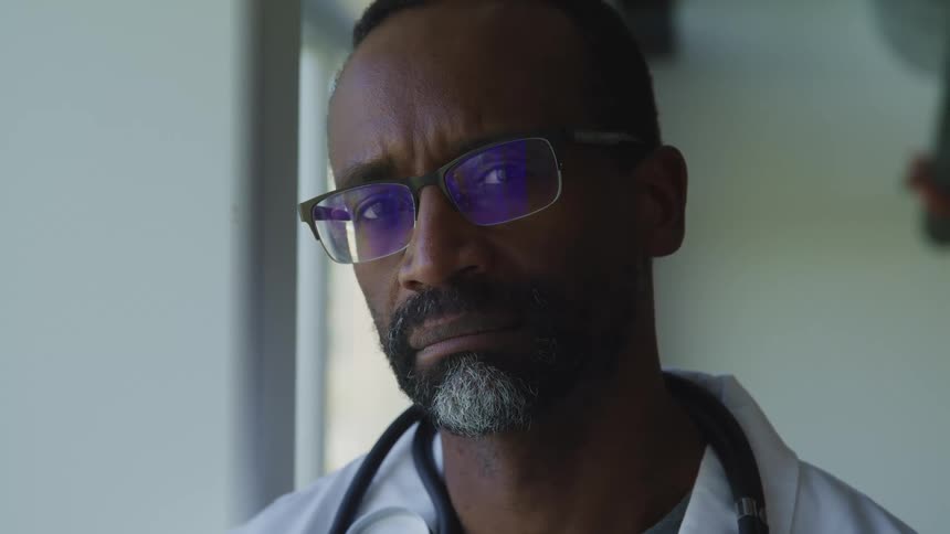 A black doctor turns his head to frown into the camera