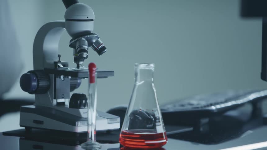 Beaker filled with red clear liquid next to a microscope in a laboratory