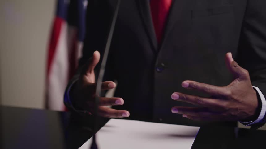 Black male standing at a podium making hand gestures