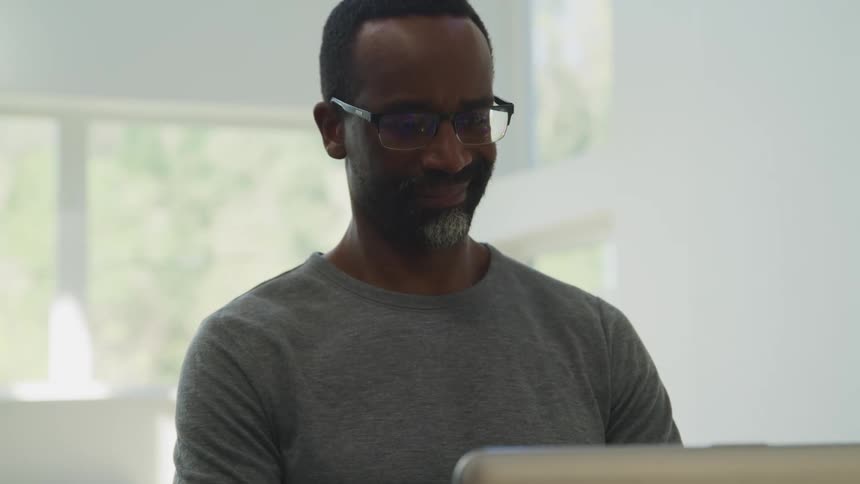 A man smiles as he uses his computer at home