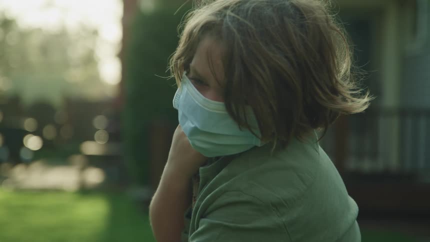 A little boy with a mask outside of his home