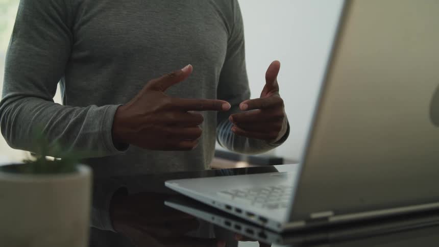 A man stands and talks with his hands while on a video call on his laptop at home