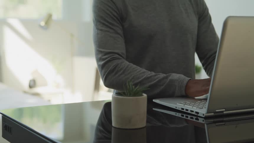 Black man with a grey sweater uses a grey laptop on a black table