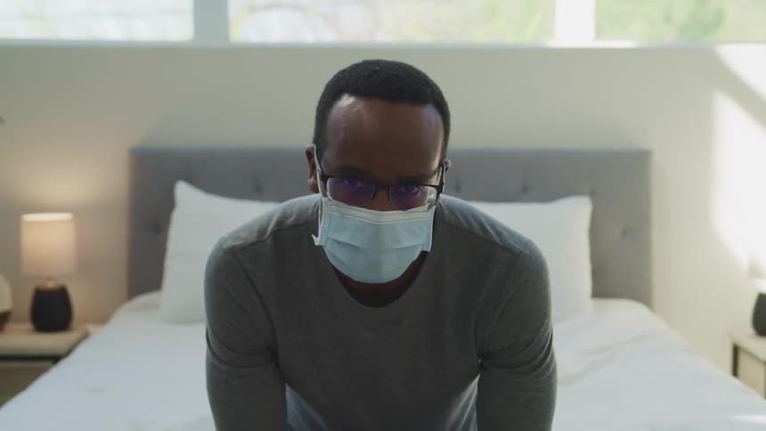 A man sitting on his bed with a mask on