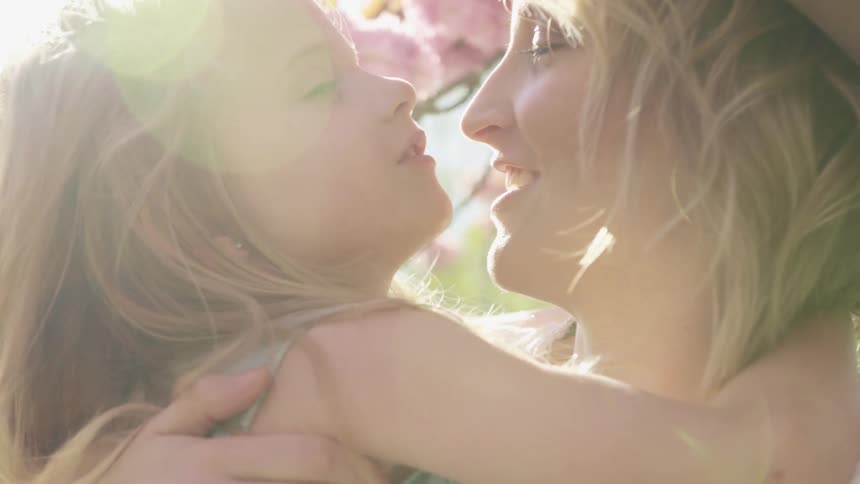 Mother and daughter hug and kiss happily on a sunny day