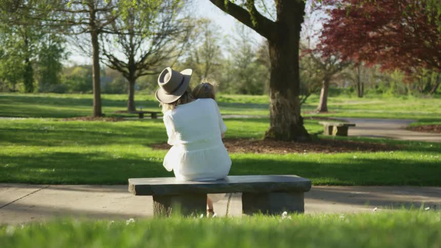 Woman sits on bench in park holding child in her lap