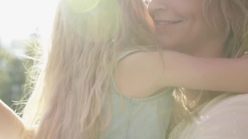A woman embraces her daughter outdoors under a sunny sky