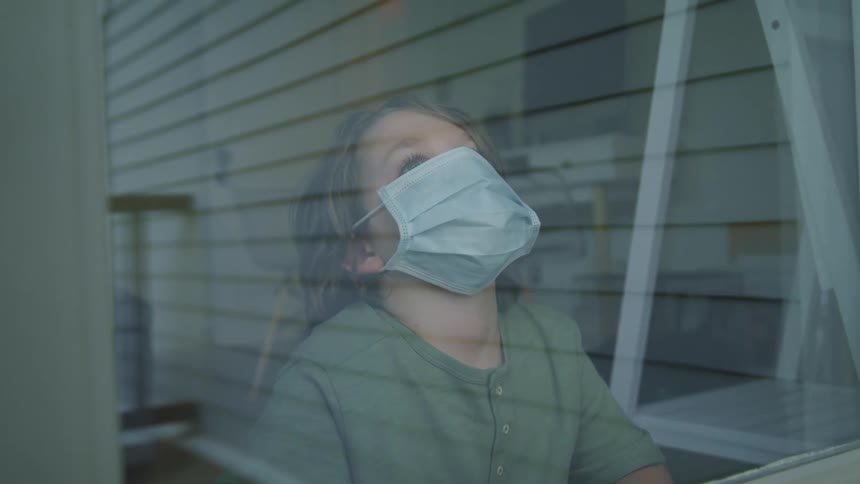 A young boy looks out a window while at home