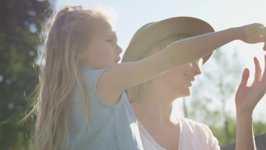 A mother is holding a child who is pointing at the forest