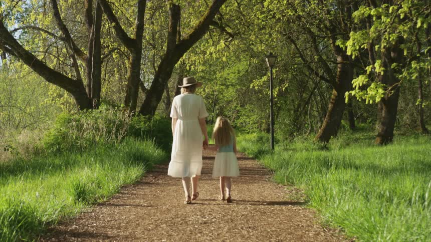 Mother and daughter walk holding hand on a gravel path through a park