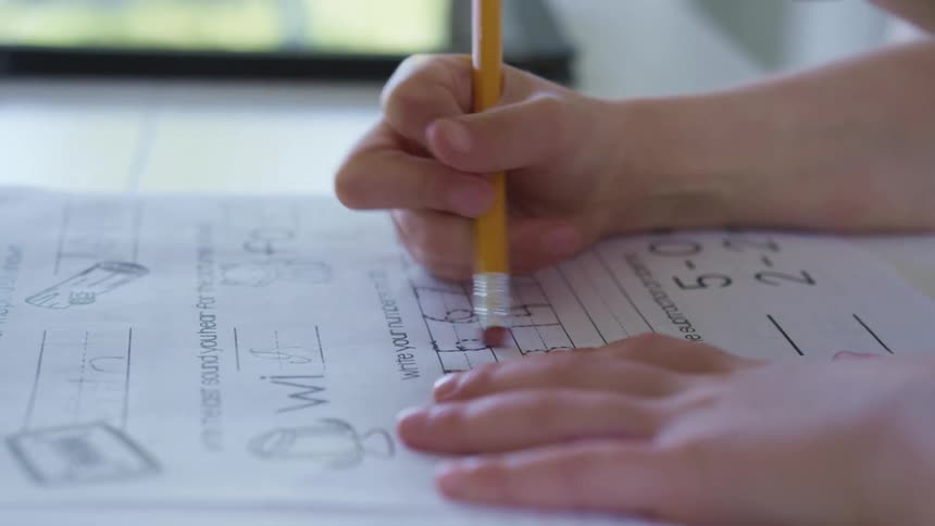 A child erases an answer on his school work as a teacher watches