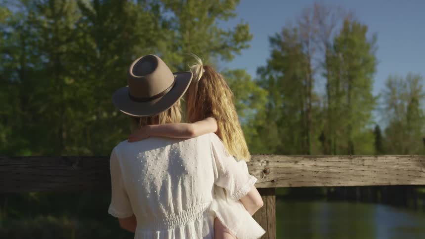A woman holds her daughter as they look at a river