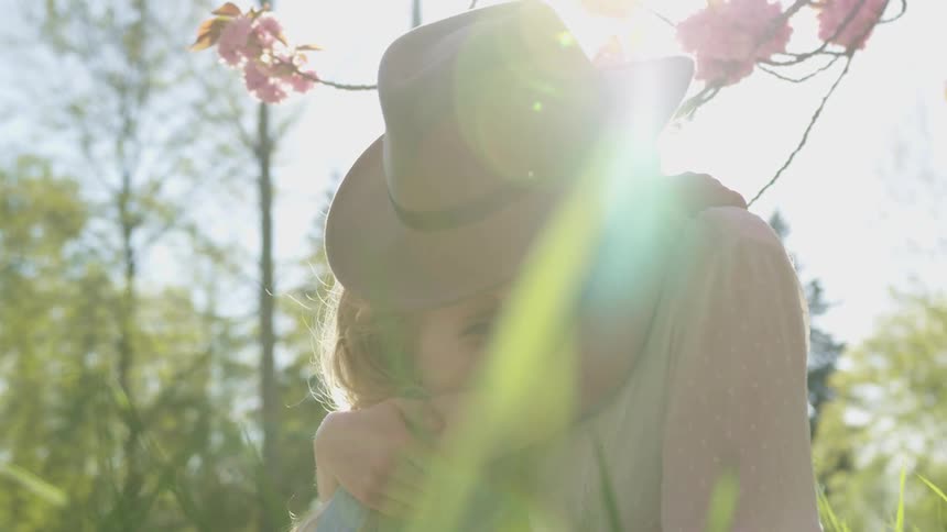 A little girl hugs her mom as they sit outside by some flowers