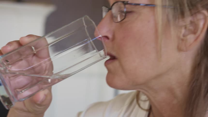 A woman drinks water after taking medication at home