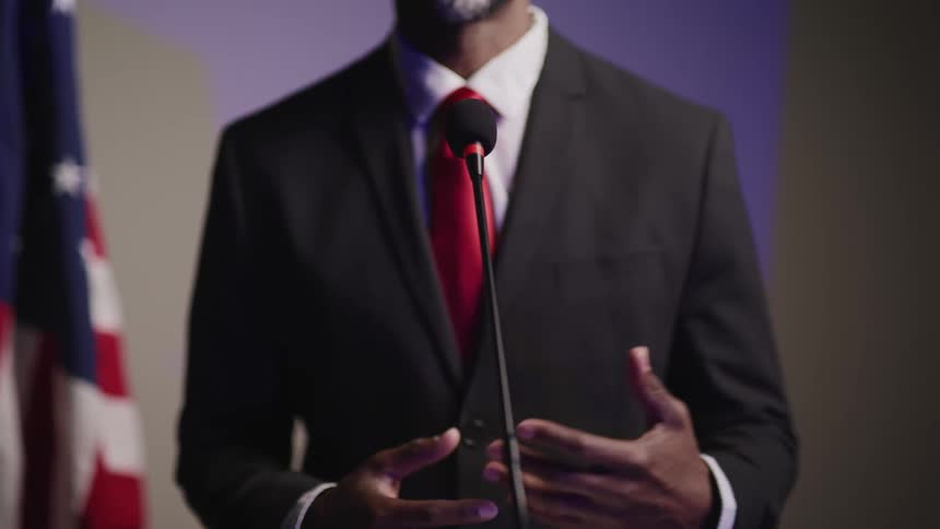 A politician speaks on a stage near an american flag