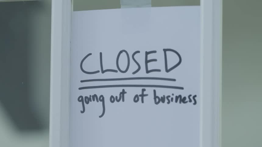 A going out of business sign is taped to a shutting door