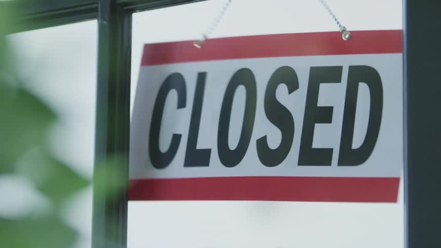 An open sign in the window of a business is flipped to the side labeled closed