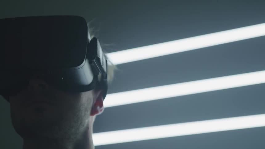 Man wearing virtual reality goggles turns head left and right in a dimly lit room