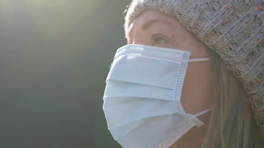 Side view of a woman with a grey beanie and a mask raises her head and looks into space