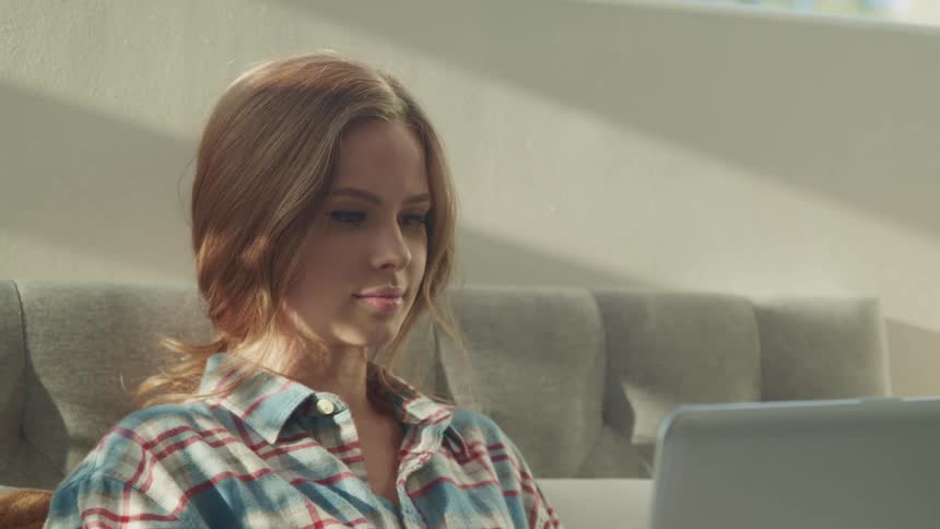 A teenager sits at home and uses her laptop