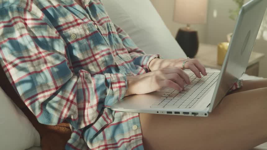 Woman types on the keyboard of a laptop while lying in bed at home