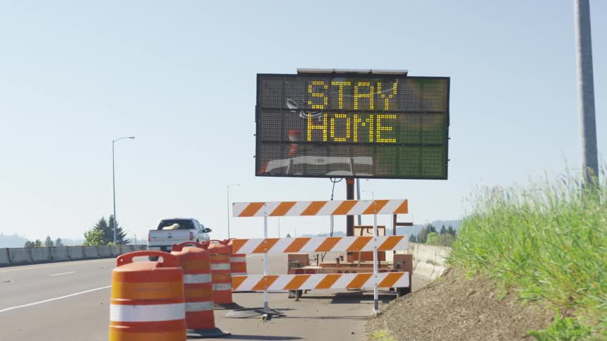 Highway traffic passes by an electronic sign urging people to stay home to save lives
