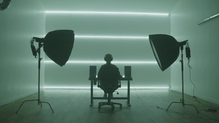 Person sits and desk near speakers under the focus of two unlit spotlights