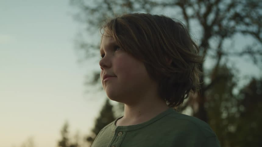 Boy with long hair and a grey t shirt looks into space in the forest