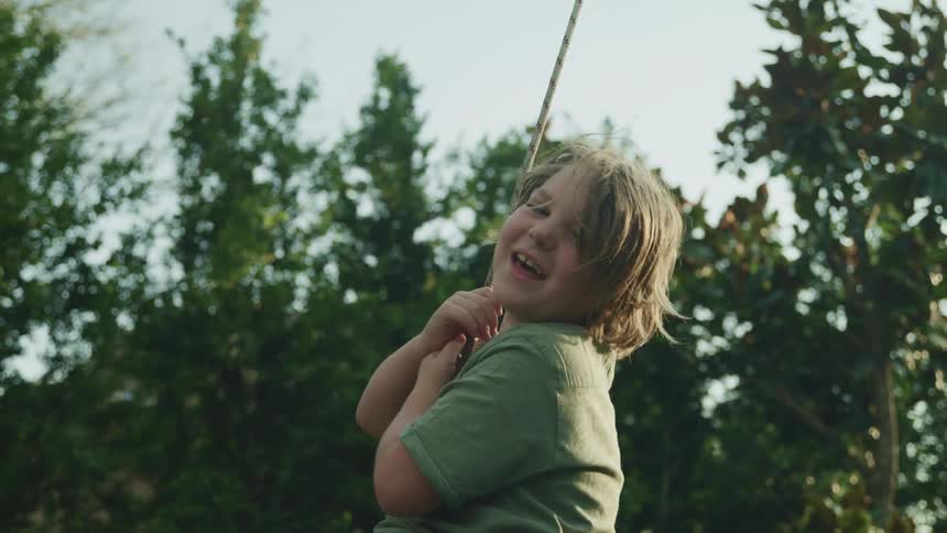 Boy swings on rope swing in field smiling