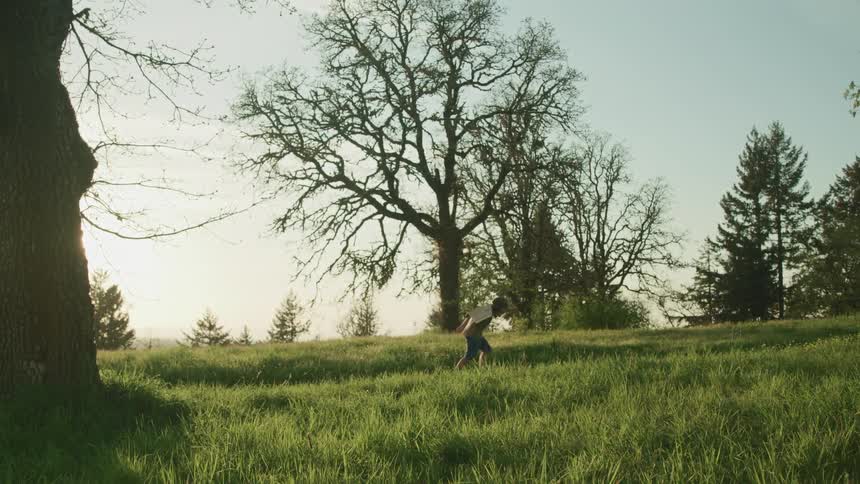 A young boy with cardboard wings pretend to be flying as he runs along a trail through a field