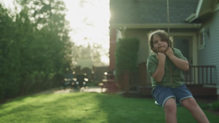 A little boy swinging outside his house