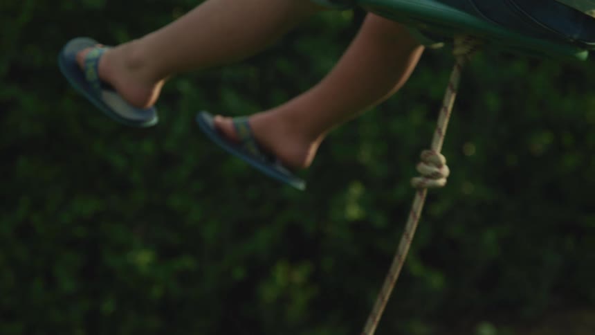 Child swings on rope swing with attached seat in field near trees