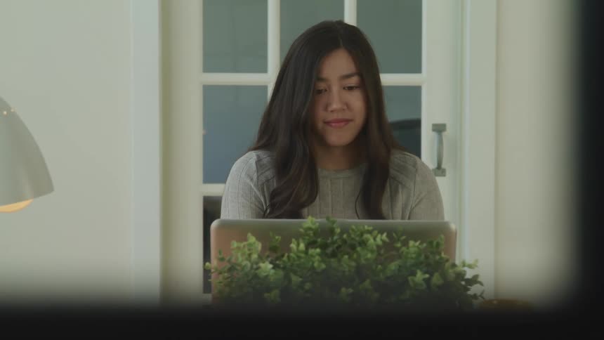 Asian woman with black long hair and sitting at the table uses a laptop