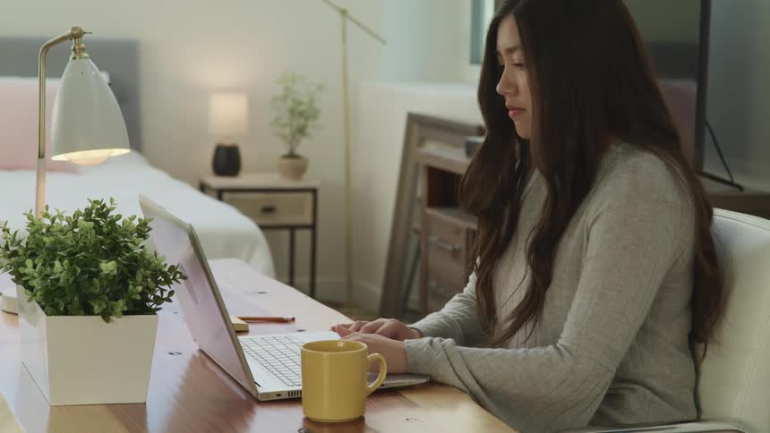 A young woman uses a laptop while sitting at a desk in a brightly lit room during the day