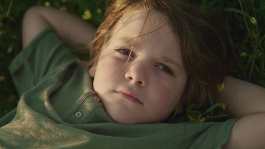 Child with long hair and a green t shirt lies down on green grass