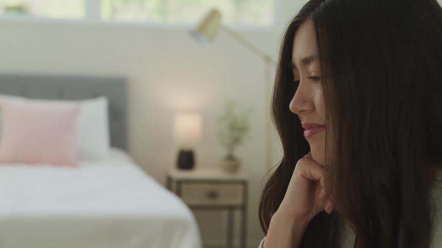 A young woman sitting in a bedroom smiles as she nods her head