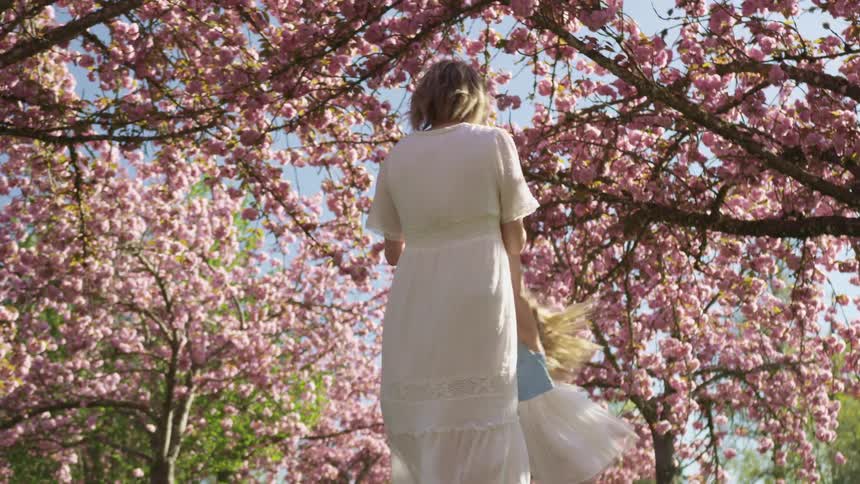 A mother swings her daughter around under cherry blossom trees