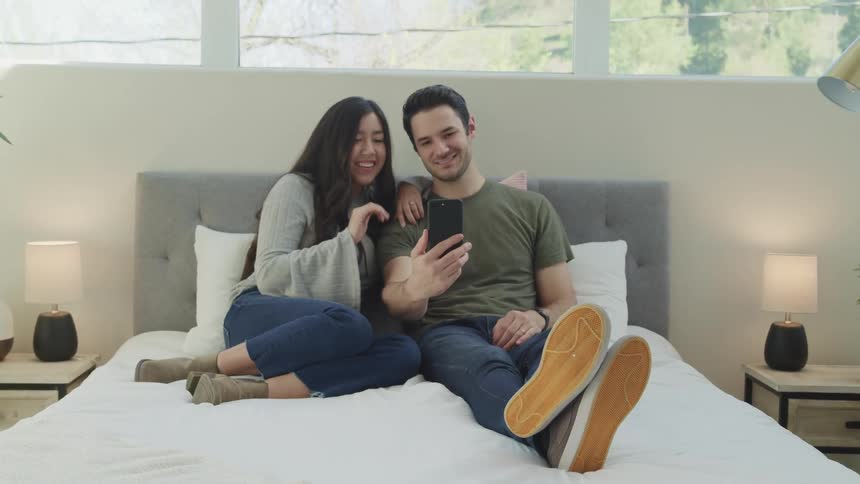 A man and woman smile and wave as they chat on a cellphone