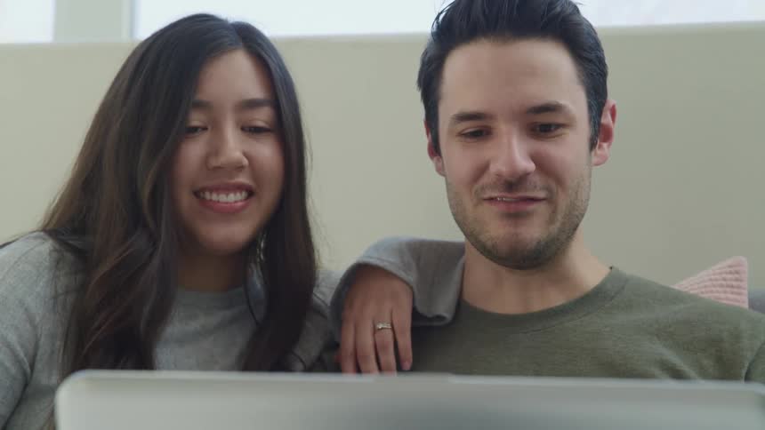 A young man and woman wave at the camera on their laptop as they video chat
