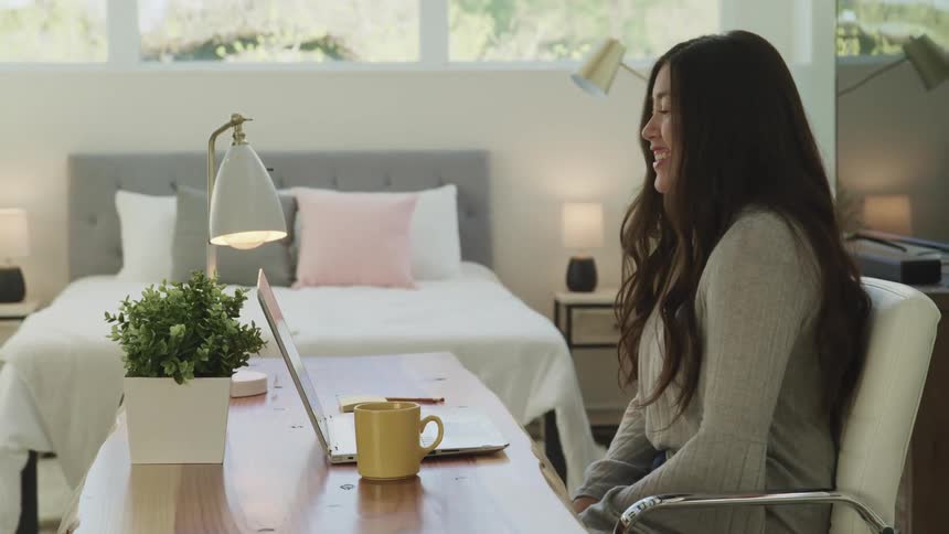 A teenager in her bedroom video chats with someone on a laptop
