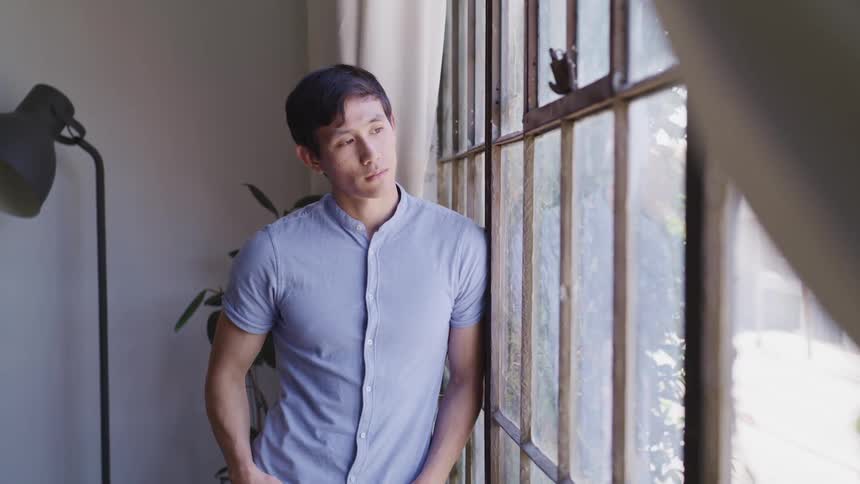 A teenage boy looks out the front window of his home