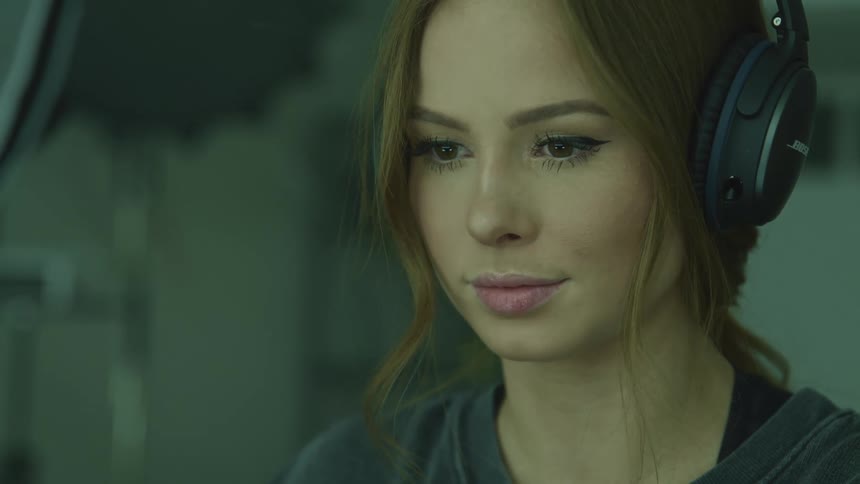 Woman with brown hair and black headphones stares down