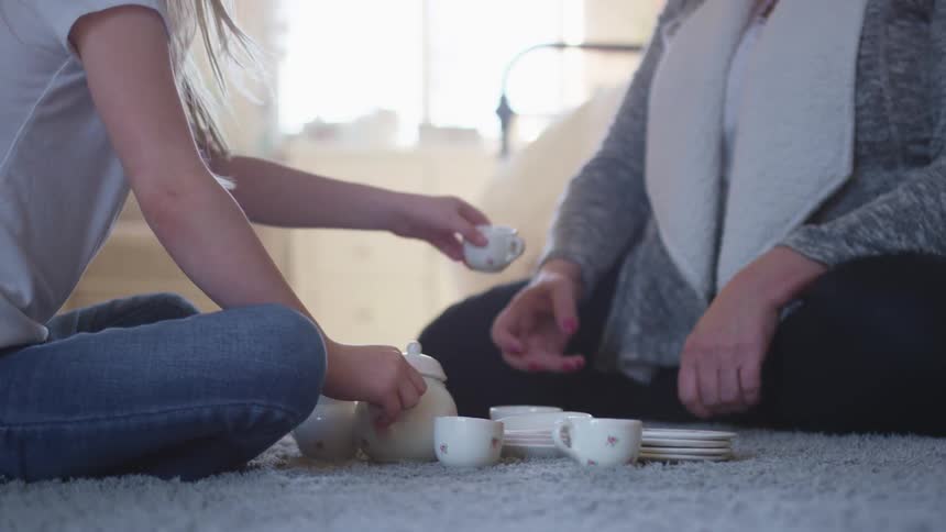 A girl pours a fake cup of tea for her mom as they have a tea party in the girls bedroom
