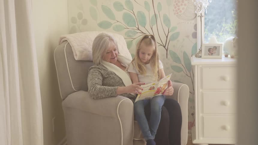 A little girl sits on her grandmothers knee as they read a book together
