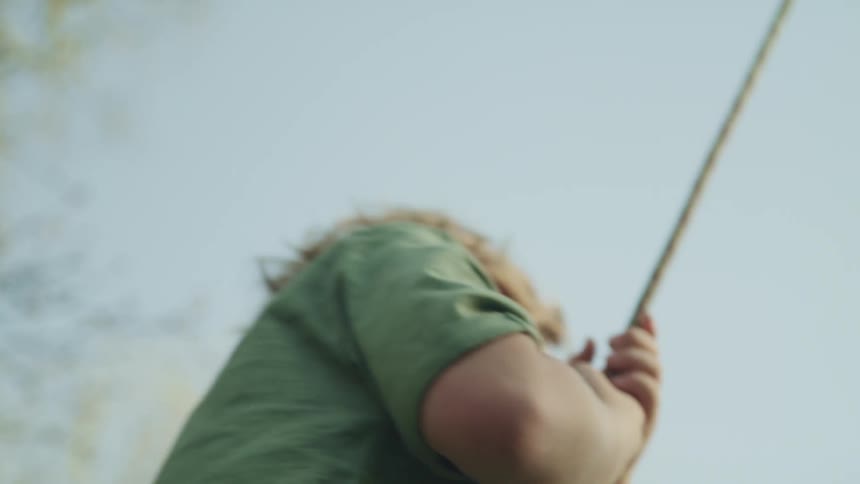Child smiles and laughs swinging on a rope swing