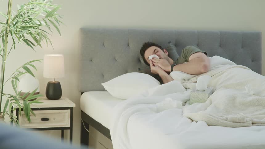 A man laying in bed wiping his nose with a tissue